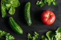 Fresh vegetables on dark background. On the table are cucumbers, tomato and fresh herbs. Ingredients for fresh salad.