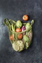 Fresh vegetables in a green string bag on a black background. Cauliflower, tomatoes, artichokes, asparagus and zucchini Royalty Free Stock Photo