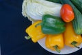 Fresh vegetables have yellow and green bell peppers, with turnips and cucumbers and tomatoes on a white plate with a black Royalty Free Stock Photo