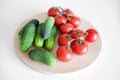 Fresh vegetables lie on a white background wooden cutting board, top view. Tomatoes on a branch, cucumbers gherkins. Royalty Free Stock Photo