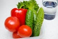 Fresh vegetables tomatoes, bell peppers, cucumbers and lettuce are in a plastic container next to a glass of water on the Royalty Free Stock Photo