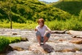 Fresh water drops. Blurred young girl with red hair sits on a stone in the river and splash water drops. Royalty Free Stock Photo