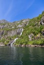 Fresh waterfalls cut through the lush, moss-covered cliffs of Trollfjorden, Lofoten