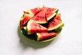 Fresh watermelon in a green plate on a white table. Slices of a watermelon in a triangular shape. Natural background with shadows