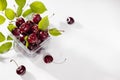 Fresh wet ripe red cherry in plastic box with green leaves, water drops on white wood board, top view, copy space, juicy summer. Royalty Free Stock Photo