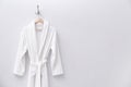 Fresh white bathrobe hanging on wall. Space for text Royalty Free Stock Photo