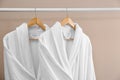 Fresh white bathrobes hanging on rack near wall Royalty Free Stock Photo