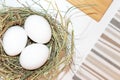 Fresh white chicken eggs in straw nest on white table, covered striped cloth Royalty Free Stock Photo