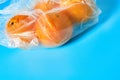 Fresh whole mandarins or oranges in polietilene bag on blue background. Fruit purchasing concept