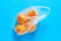 Fresh whole mandarins or oranges in polietilene bag on blue background. Fruit purchasing concept. Top view