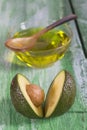 Fresh whole and sliced avocado and a cup of oil ongreen craked wooden table- cooking, healthcare concept