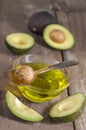 Fresh whole and sliced avocado and a cup of oil ongreen craked wooden table- cooking, spa, bodycare concept