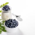 Fresh wild forest blueberries in white bowl and natural yogurt in glass jar on white. Copy space Royalty Free Stock Photo