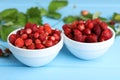 Fresh wild strawberries in bowls on light blue table Royalty Free Stock Photo