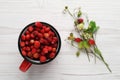 Fresh wild strawberries in mug near stems with flowers and leaves on white wooden table, flat lay Royalty Free Stock Photo