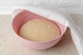 Fresh yeast dough rising in a large plastic bowl covered with white linen towel on the kitchen table. Hands preparing dough for Royalty Free Stock Photo