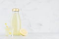 Fresh yellow lemon juice in glass bottle mock up with straw, wine glass, fruit slice on white wood table in light interior. Royalty Free Stock Photo