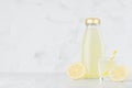 Fresh yellow lemon juice in glass bottle mock up with straw, wine glass, fruit slice on white wood table in light interior. Royalty Free Stock Photo