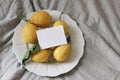 Fresh yellow lemons, leaves on white ceramic plate. Business card mockup. Greige muslin tablecloth, fabric. Closeup of