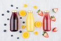 Fresh yellow orange, pink strawberry and violet blueberry juices in glass bottles with fruit ingredients on white wood board.