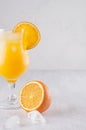 Fresh yellow oranges cocktail in elegance wineglass with ice cubes, straw and half oranges on soft white wood background. Royalty Free Stock Photo