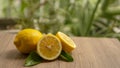 Fresh yellow ripe lemon round fruit and half sliced fruits with green leaf on brown wooden, blurry green tree background Royalty Free Stock Photo