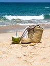 A fresh young coconut is ready to eat and a straw bag and a women`s straw hat on a sandy beach against a blue sea. Tropical Royalty Free Stock Photo