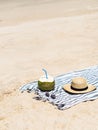 A fresh young coconut is ready to eat and a women`s straw hat on a towel on a sandy beach. Tropical vacation travel concept. Copy Royalty Free Stock Photo