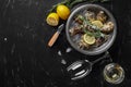 Fresh closed oysters, ice, lemon on a round metal plate and champagne are on a black stone textured background. Top view