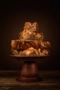 freshly baked apple pie stacked in several layers on clay cake stand on plank table against blurred brown backdrop with light Royalty Free Stock Photo