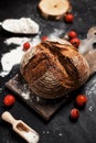 Freshly baked bread, flour and tomatoes on a wooden board on a table