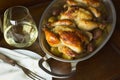 Two Cornish hens in an aluminum baking pan with handles on a wooden table, shown with a glass of white wine. Royalty Free Stock Photo