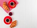 Freshly baked croissant on napkin, cup of coffee in red cup on white wooden background. French breakfast. Fresh pastries for break Royalty Free Stock Photo