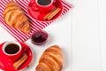 Freshly baked croissant on napkin, cup of coffee in red cup on white wooden background. French breakfast. Fresh pastries for break Royalty Free Stock Photo