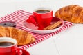 Freshly baked croissant on napkin, cup of coffee in red cup on white wooden background. French breakfast. Fresh pastries for break Royalty Free Stock Photo