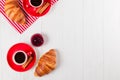 Freshly baked croissant on napkin, cup of coffee in red cup on white wooden background. French breakfast. Fresh pastries for break Royalty Free Stock Photo