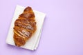 Freshly baked croissant with sugar powder on a purple background with copy space. Concept of a cafe advertisement.