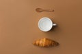 Freshly baked French buttery flaky croissant empty cup for tea or coffee wooden spoon on brown tabletop background. Knolling