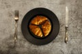 Freshly baked French croissants on a black plate with a fork and knife on a gray concrete background. View from above. Royalty Free Stock Photo