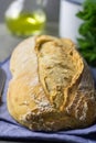 Freshly Baked Hand Crafted Rustic Bread Loaf on Blue Linen Towel on Dark Kitchen Table Knife Green Herbs Bottle of Olive Oil Royalty Free Stock Photo
