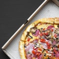 Freshly baked pizza in a cardboard box on black background, overhead view. Flat lay, top view, from above Royalty Free Stock Photo
