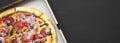 Freshly baked pizza in a cardboard box on black surface, overhead view. Flat lay, from above. Space for text Royalty Free Stock Photo