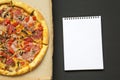 Freshly baked pizza in a cardboard box with notebook over black background, top view. Royalty Free Stock Photo
