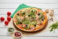 Freshly baked pizza with ham, rukkola, sauce pesto and olives served on wooden background with tomatoes, sauces and herbs. Food Royalty Free Stock Photo