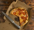 freshly baked pizza with mushrooms and ham in a cardboard box with a kitchen knife on a wooden table Royalty Free Stock Photo