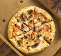 freshly baked pizza with mushrooms and ham in a cardboard box on a wooden table Royalty Free Stock Photo