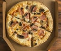 freshly baked pizza with mushrooms and ham in a cardboard box on a wooden table Royalty Free Stock Photo