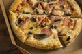 freshly baked pizza with mushrooms and ham in a cardboard box on a wooden table Royalty Free Stock Photo