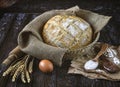 Freshly baked rye bread with flax seeds in a burlap basket, wooden spoons with flour, wheat ears, egg. Royalty Free Stock Photo