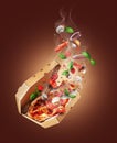 Freshly baked spicy pizza with various food ingredients in the air on a brown background